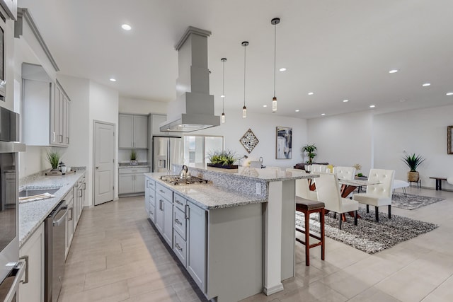 kitchen featuring a breakfast bar area, light stone counters, gray cabinets, exhaust hood, and stainless steel appliances