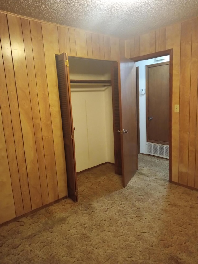 corridor featuring a textured ceiling, wood walls, and light carpet