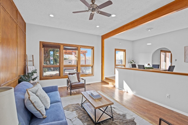 living room featuring beamed ceiling, a textured ceiling, light hardwood / wood-style flooring, and ceiling fan