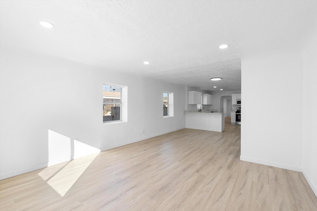 unfurnished living room with light wood-type flooring, sink, and a textured ceiling