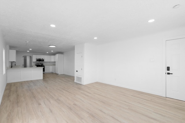 unfurnished living room with sink, a textured ceiling, and light hardwood / wood-style floors