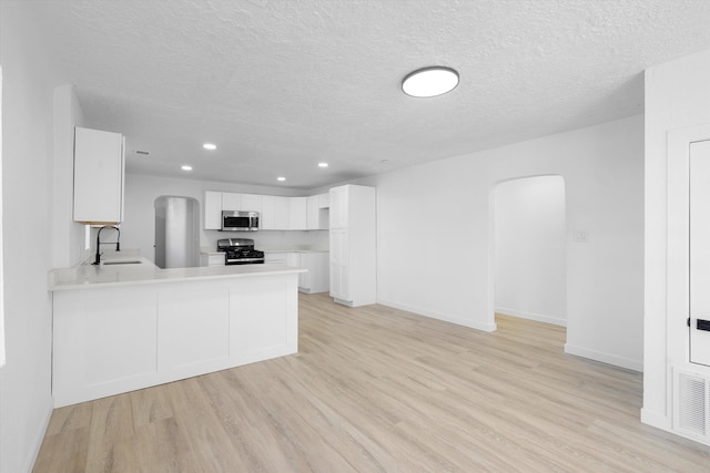 kitchen with kitchen peninsula, sink, stainless steel appliances, a textured ceiling, and white cabinets