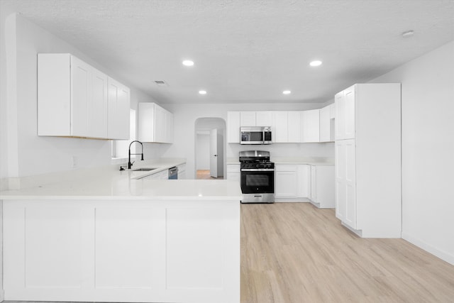 kitchen with kitchen peninsula, stainless steel appliances, a textured ceiling, white cabinets, and sink