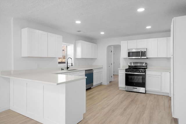 kitchen with kitchen peninsula, sink, appliances with stainless steel finishes, a textured ceiling, and white cabinets