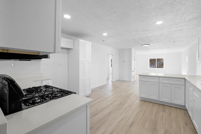 kitchen featuring a textured ceiling, gas stove, white cabinetry, kitchen peninsula, and light hardwood / wood-style flooring