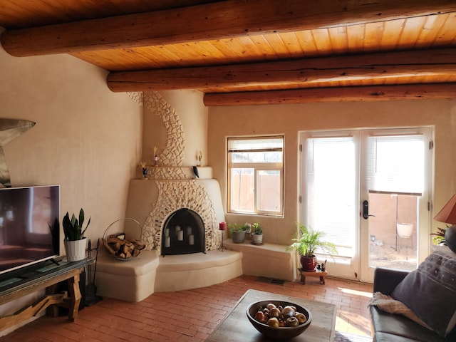 living room featuring beam ceiling, plenty of natural light, wooden ceiling, a fireplace, and brick floor