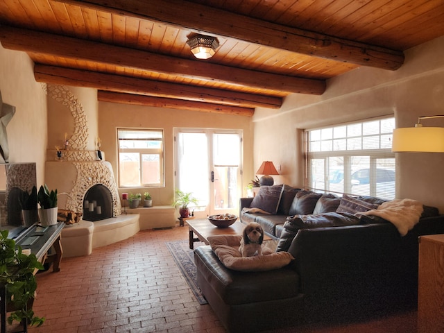 living room featuring wood ceiling, a stone fireplace, a healthy amount of sunlight, and beam ceiling