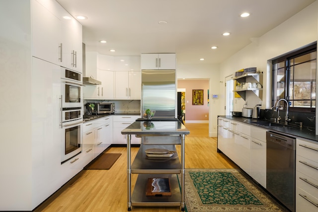 kitchen with sink, white cabinets, light wood-type flooring, decorative backsplash, and appliances with stainless steel finishes