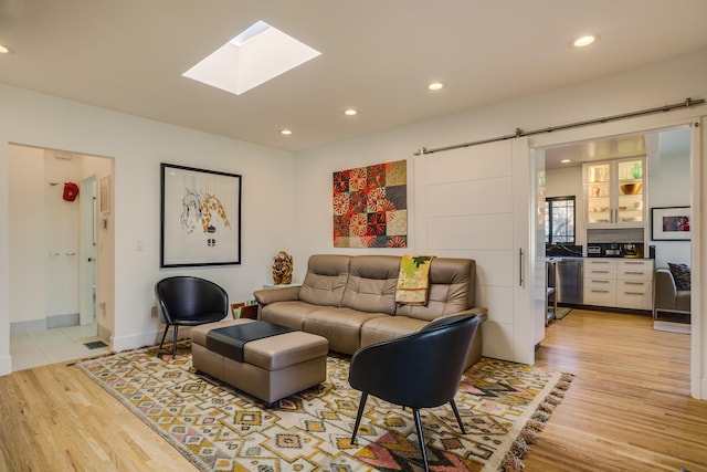 living room featuring a skylight, a barn door, and light hardwood / wood-style flooring