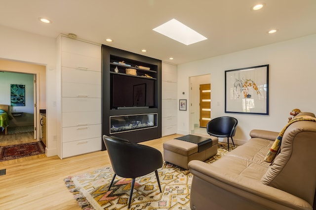 living room with a skylight, built in shelves, and light hardwood / wood-style flooring