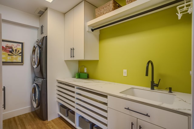 washroom with stacked washer and dryer, sink, light wood-type flooring, and cabinets