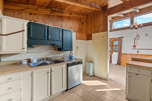 kitchen featuring radiator, wooden walls, white cabinetry, sink, and stainless steel dishwasher