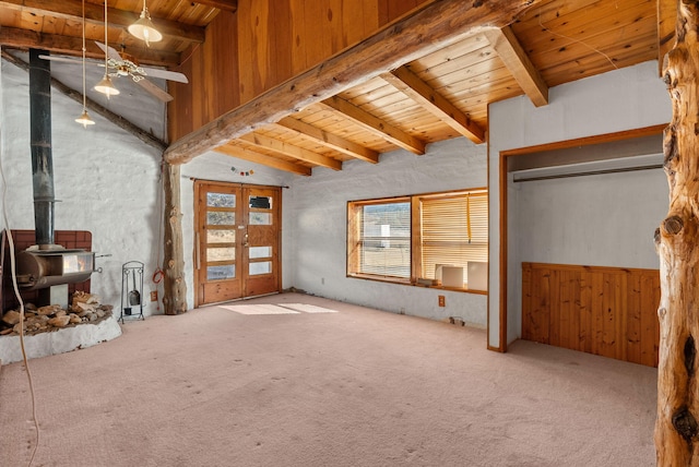 unfurnished living room with wooden walls, carpet floors, a wood stove, vaulted ceiling with beams, and wood ceiling