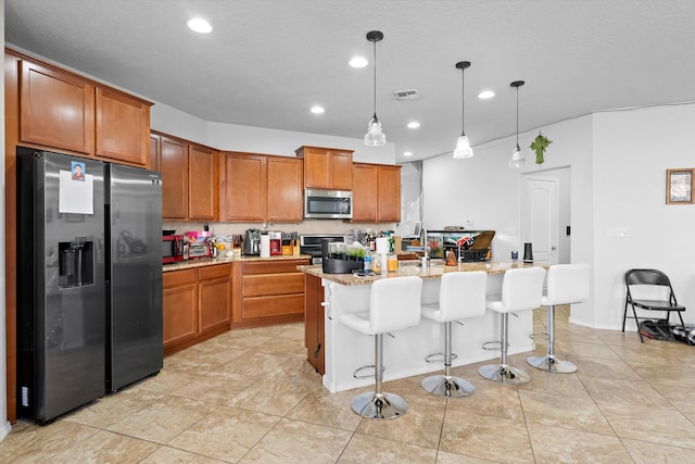 kitchen with a center island with sink, appliances with stainless steel finishes, decorative light fixtures, a kitchen breakfast bar, and a textured ceiling