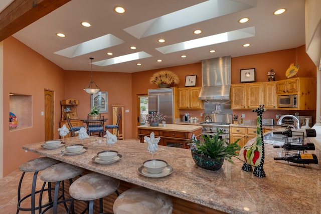 kitchen featuring built in appliances, light stone counters, a spacious island, wall chimney range hood, and a skylight