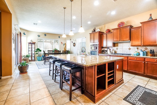 kitchen with a breakfast bar area, hanging light fixtures, stainless steel appliances, an island with sink, and a textured ceiling