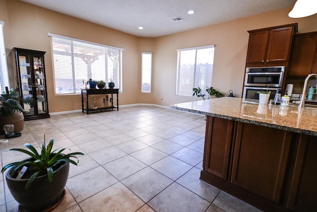 kitchen featuring light stone counters, stainless steel double oven, light tile patterned flooring, visible vents, and baseboards