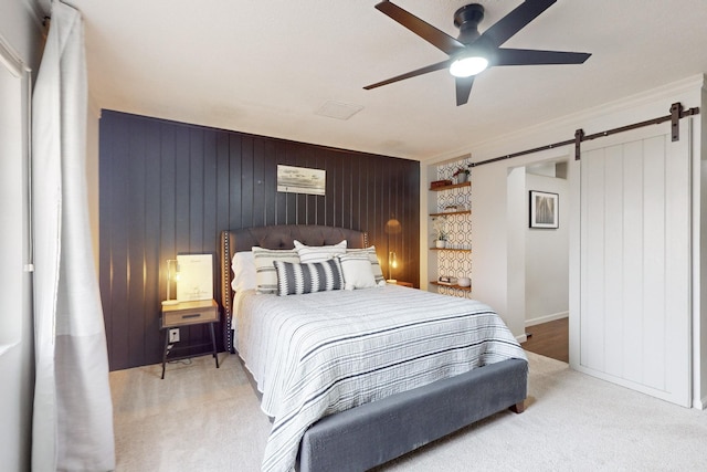 bedroom with a barn door, wood walls, ceiling fan, light colored carpet, and crown molding