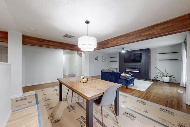 dining area featuring ceiling fan, light hardwood / wood-style flooring, beamed ceiling, and a fireplace