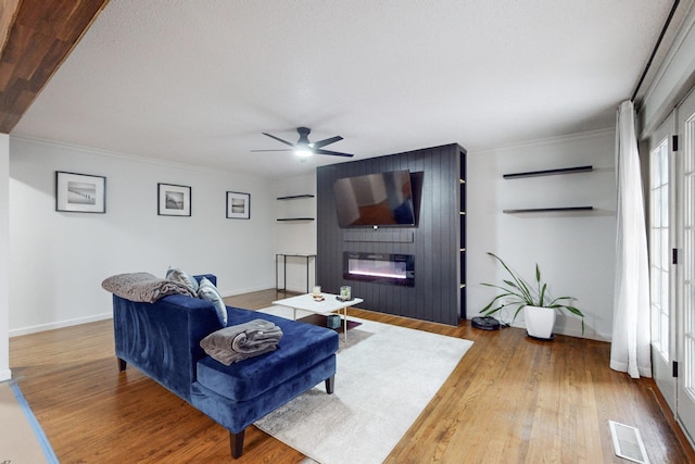 living room with hardwood / wood-style flooring, a large fireplace, ornamental molding, and ceiling fan