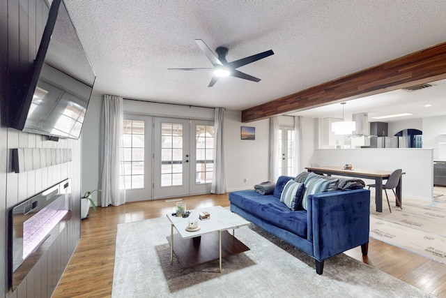 living room featuring beam ceiling, french doors, a textured ceiling, and light hardwood / wood-style flooring