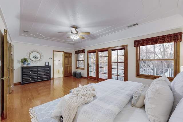 bedroom with ceiling fan, connected bathroom, a raised ceiling, and wood-type flooring