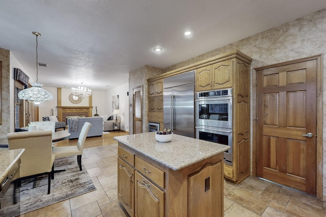 kitchen featuring a center island, a brick fireplace, a chandelier, pendant lighting, and appliances with stainless steel finishes