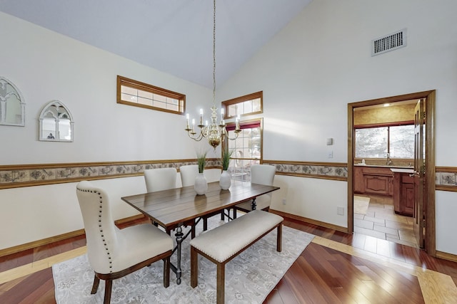 dining space featuring high vaulted ceiling, a chandelier, a wealth of natural light, and hardwood / wood-style floors