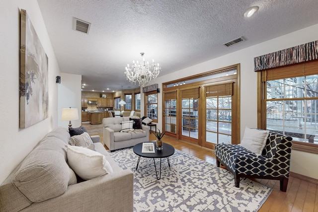 living room featuring an inviting chandelier, light wood-type flooring, and a textured ceiling