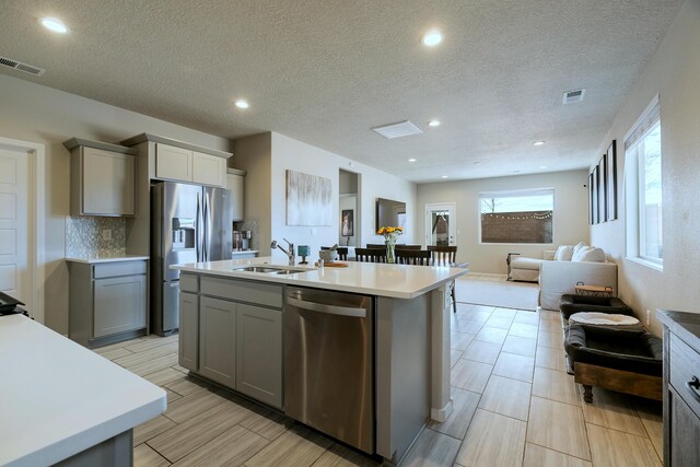 kitchen featuring gray cabinetry, an island with sink, appliances with stainless steel finishes, and sink