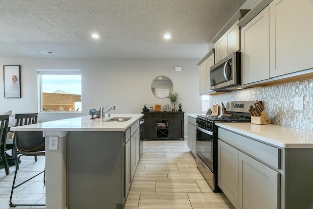 kitchen with a breakfast bar, a kitchen island with sink, gray cabinetry, appliances with stainless steel finishes, and sink