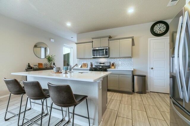 kitchen featuring a center island with sink, appliances with stainless steel finishes, gray cabinets, and sink