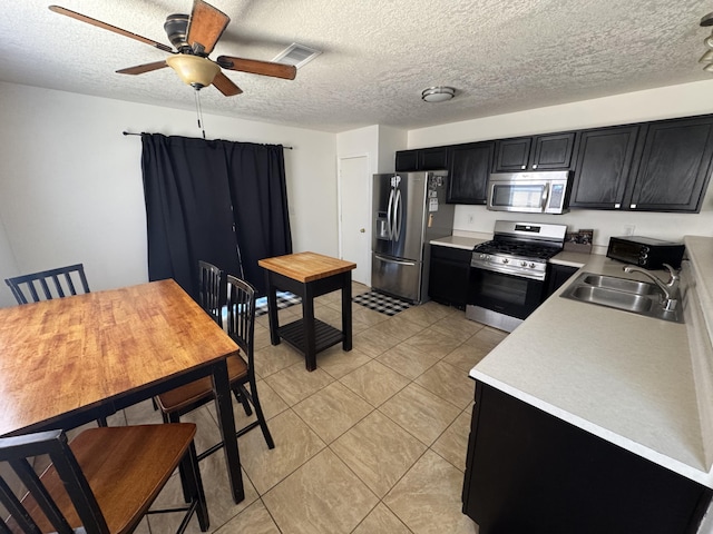 kitchen featuring a textured ceiling, appliances with stainless steel finishes, sink, ceiling fan, and light tile patterned floors