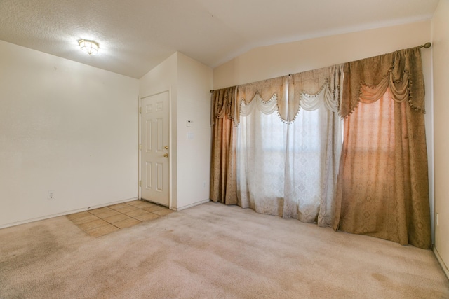 unfurnished room with a textured ceiling, lofted ceiling, and carpet