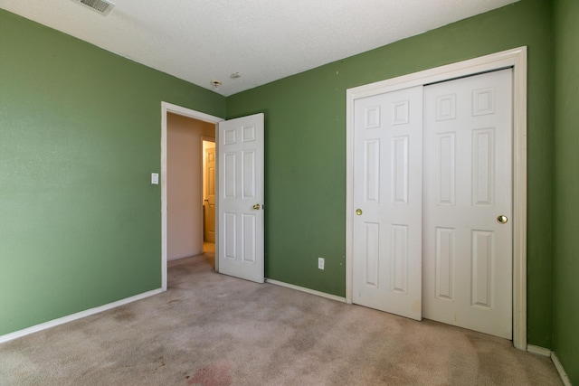 unfurnished bedroom featuring light colored carpet, a closet, and a textured ceiling