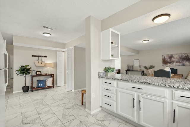 kitchen featuring white cabinets, a textured ceiling, and light stone countertops