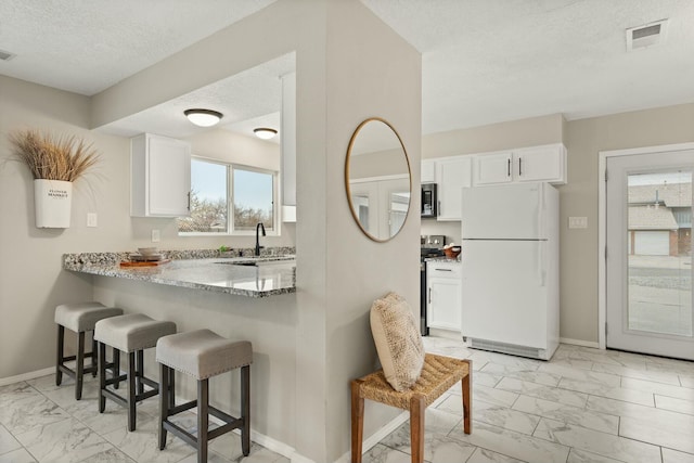 kitchen with light stone counters, white cabinets, appliances with stainless steel finishes, and a kitchen bar