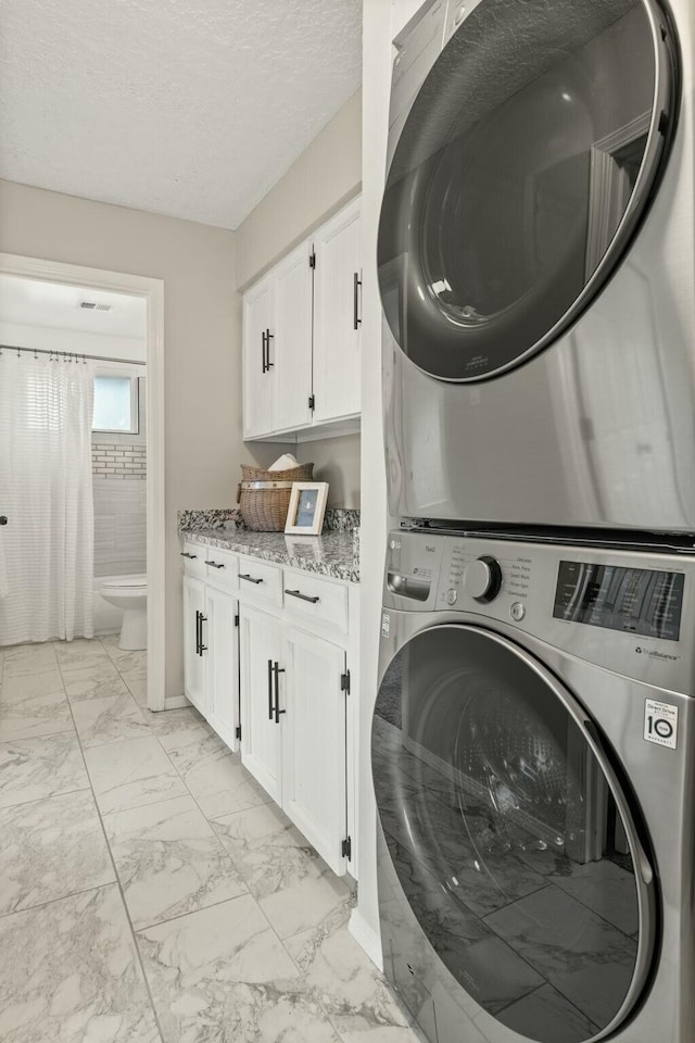 laundry area featuring cabinets, a textured ceiling, and stacked washer / dryer