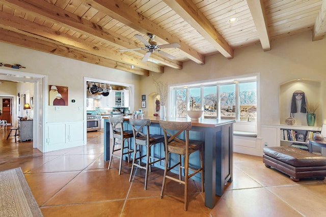 kitchen featuring a center island, stainless steel stove, light tile patterned floors, a breakfast bar, and beam ceiling