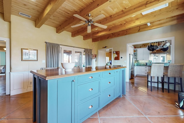 kitchen with beamed ceiling, a kitchen breakfast bar, blue cabinetry, stainless steel fridge, and wood ceiling