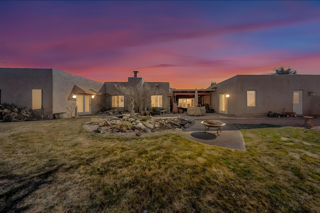 back house at dusk featuring a patio, a yard, and a fire pit