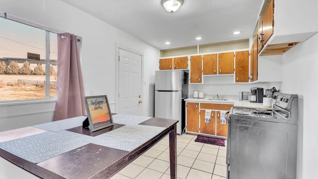 kitchen featuring light tile patterned floors, stove, sink, and stainless steel refrigerator