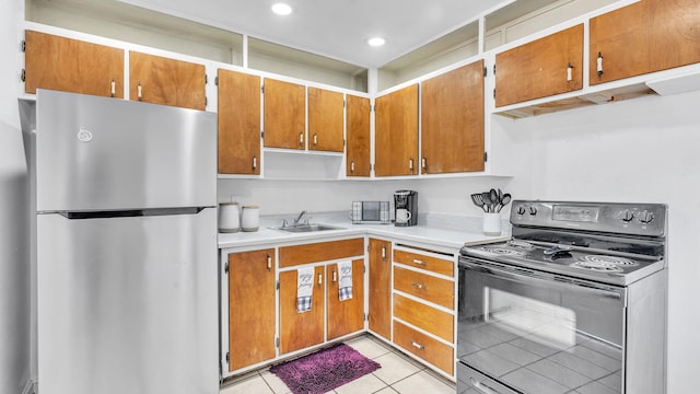 kitchen with light tile patterned floors, black range with electric stovetop, freestanding refrigerator, light countertops, and a sink