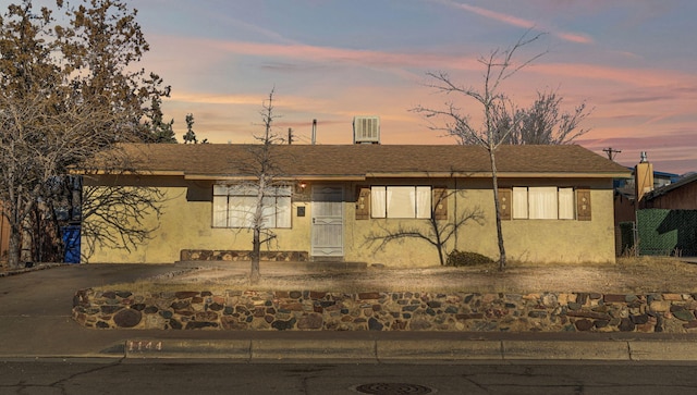 ranch-style house featuring a shingled roof, central AC unit, and stucco siding