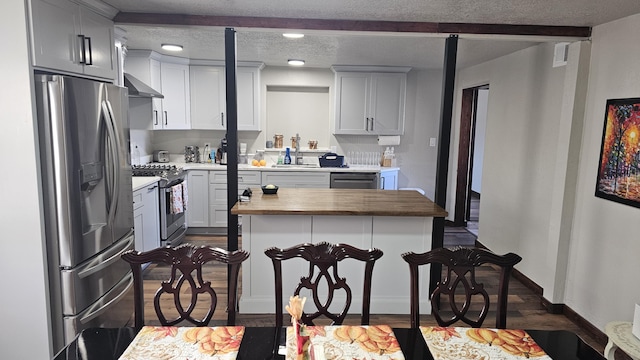 kitchen with a textured ceiling, a kitchen bar, dark hardwood / wood-style flooring, butcher block counters, and stainless steel appliances