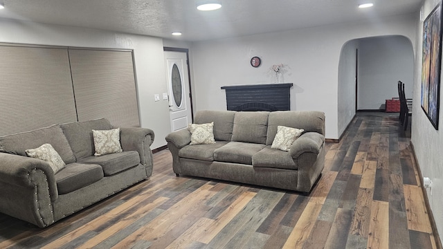 living room with a textured ceiling, dark wood-type flooring, and a brick fireplace