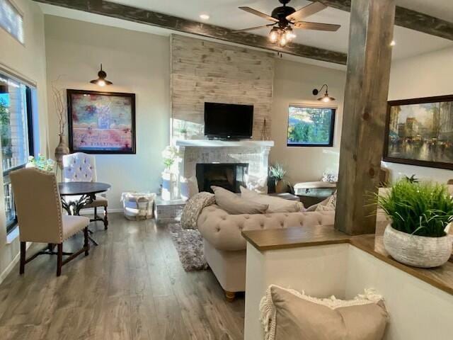 living room with ceiling fan, a fireplace, beamed ceiling, and hardwood / wood-style flooring