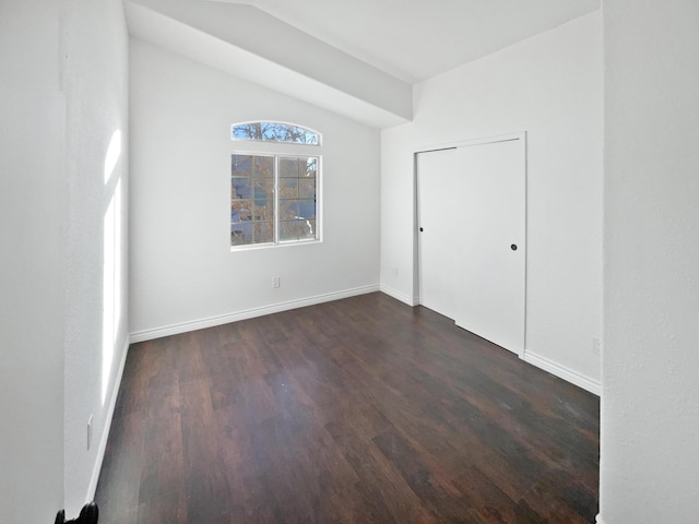 empty room featuring vaulted ceiling and dark hardwood / wood-style flooring