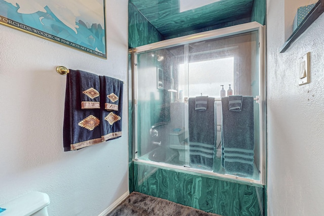 bathroom with toilet and bath / shower combo with glass door