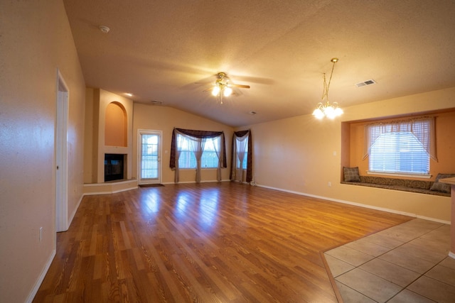 unfurnished living room featuring lofted ceiling, light hardwood / wood-style flooring, a fireplace, a textured ceiling, and ceiling fan with notable chandelier